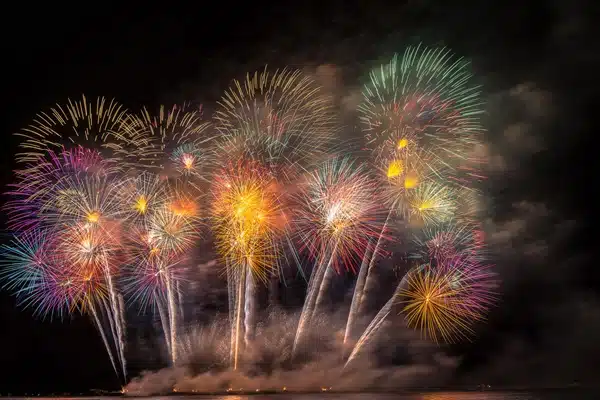 A vibrant fireworks display, celebrating Diwali 2024—the Festival of Lights—lights up the night sky with various colors and patterns above a shimmering body of water.