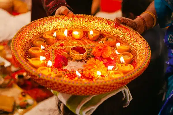 A decorated platter with lit oil lamps and flowers, held by a person in traditional clothing, shines brightly during the Festival of Lights on Diwali 2022, adding grace to this vibrant cultural celebration.