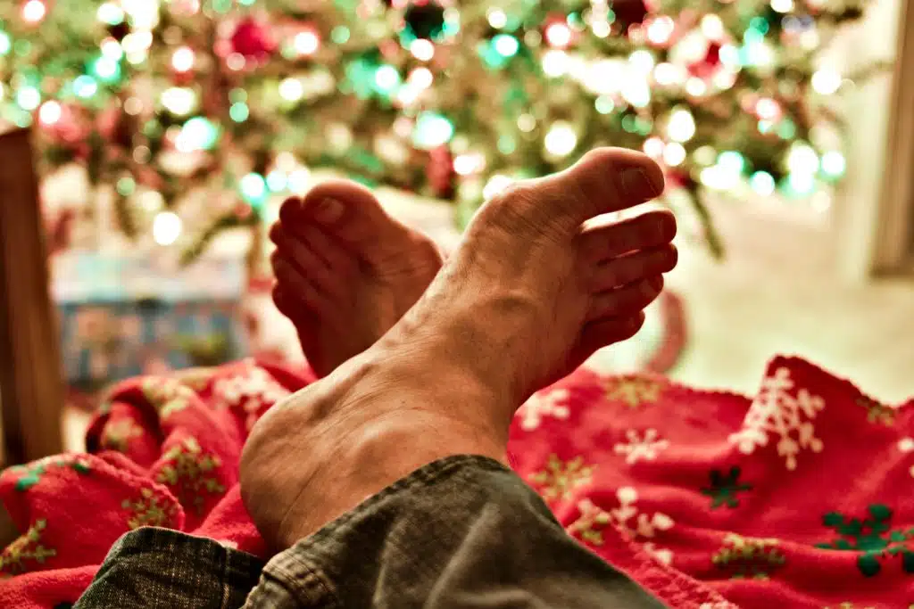 the man with these two bare feet in front of a Christmas tree considers whether to drive barefoot