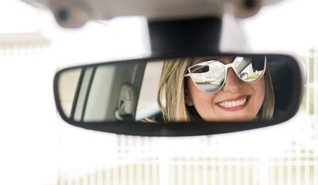 women smiles in rear view mirror after roadside assist helps get her locked keys from inside her car