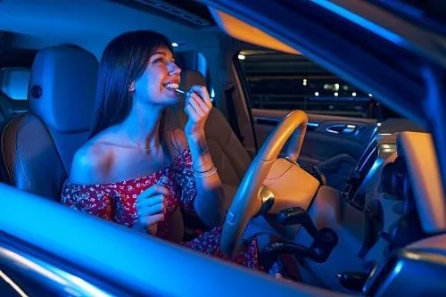 Cheerful young woman doing makeup in car. Is she from a state with the worst driver's in Australia?