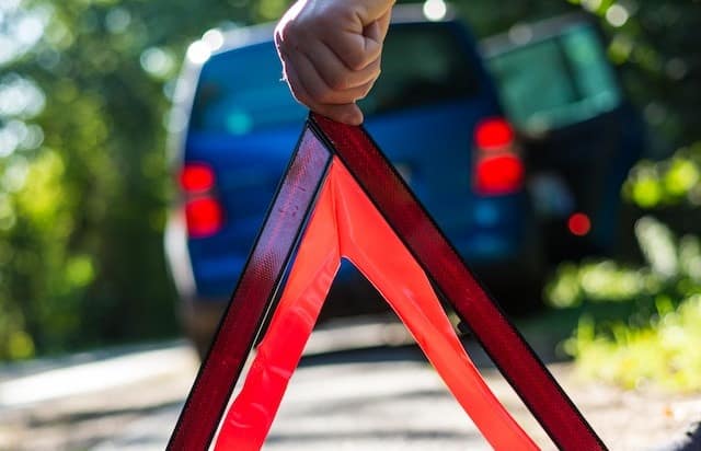 man puts up his emergency triangle after a car breakdown while waiting for roadside assistance