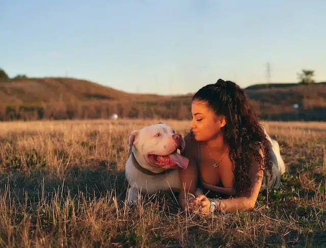 a pet owner lies in a field with her dog helping to calm it down from anxiety