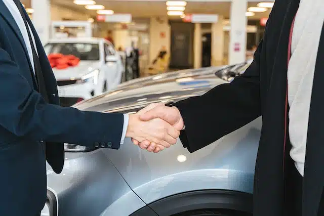 a man shakes the car dealer's hand to confirm his decision to buy a runout model car