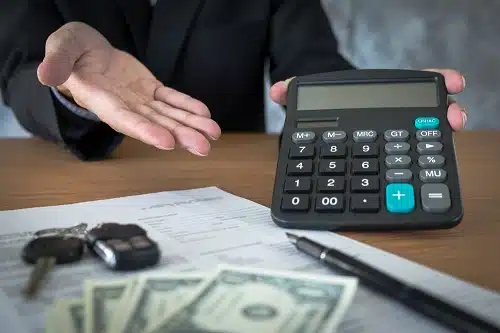 Car salesman holding a key and calculating a price at the dealership office. You may be wondering about affordable cars and what car can I afford