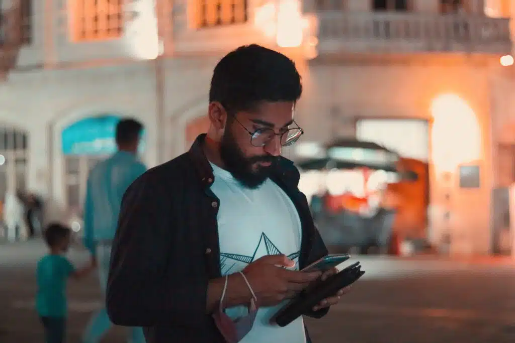 Indian man in white shirt looking at phone, calling police because his car got stolen