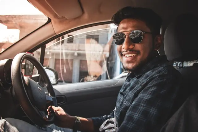 A man with a smile on his face driving a car, wondering about high or low excess in car insurance.