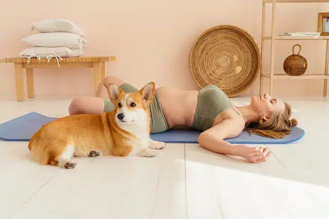 a woman practices yoga with her dog alongside her