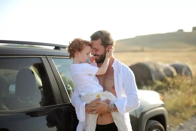 A man hugs his little girl happily feeling peace of mind thanks to having car insurance cover for their family road trip.