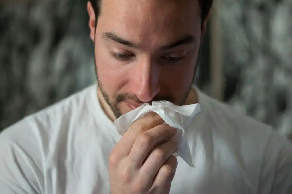 This man in a white t-shirt is experiencing symptoms of being allergic to cats.
