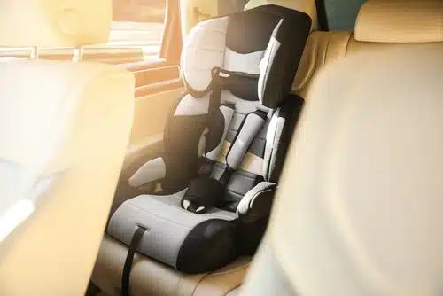 The child car seat is securely installed in the backseat of a vehicle with beige interiors, basking in warm sunlight—a perfect blend of safety and style, offering an optional benefit for peace of mind on every journey.