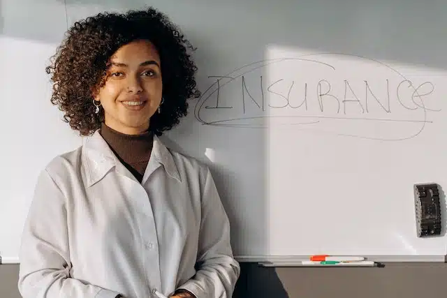A woman with a whiteboard that says 'insurance' is explaining how to reduce the cost of car insurance to her clients
