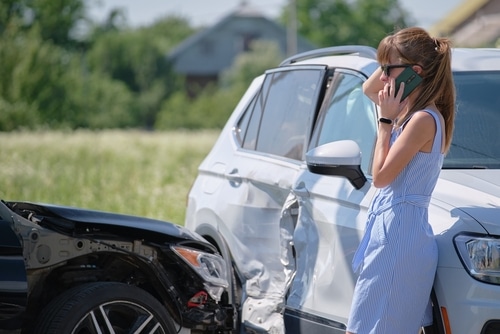 A woman standing next to a wrecked car, filing a Third Party Property Damage insurance claim in Australia.