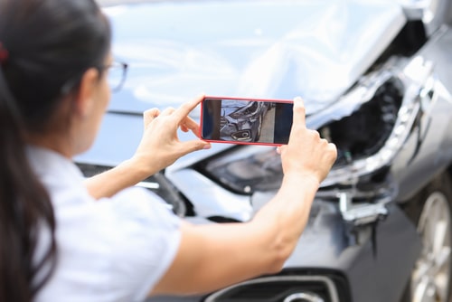 A woman taking a picture of a damaged car resulting from third-party property damage.