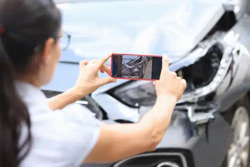 A woman taking a picture of a damaged car resulting from third-party property damage.