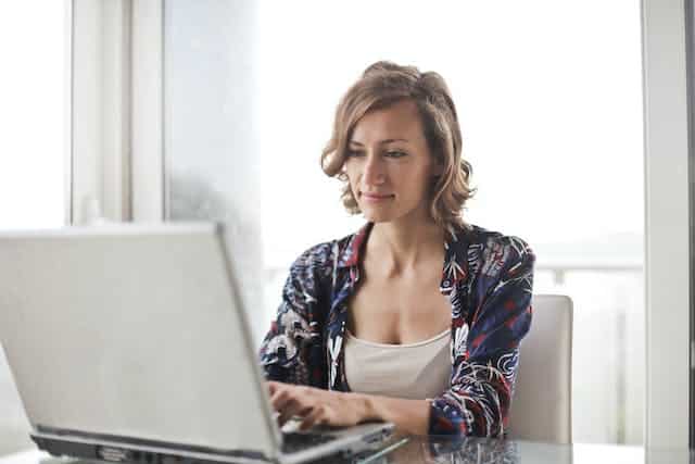 A woman sitting at a table using a laptop to process her car insurance claim after being involved in an at-fault car accident where the other driver doesn't have insurance.