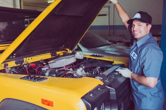 A mechanic working on a yellow truck in a garage, ensuring optimal car visibility.