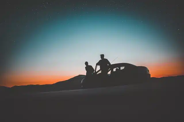 Two people standing in front of their vehicle taking a break on a road trip to admire the Australian sunset.