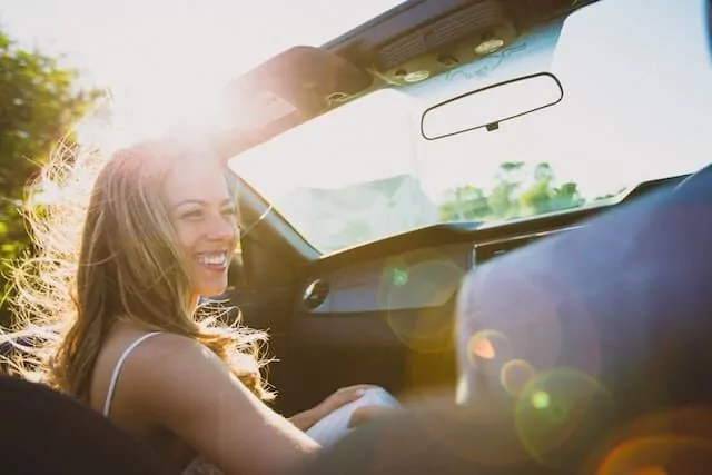 A woman smiling in passengers seat of an open topped car.