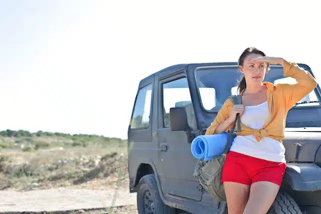 A woman standing next to a car on a beach stop-off during her summer car trip