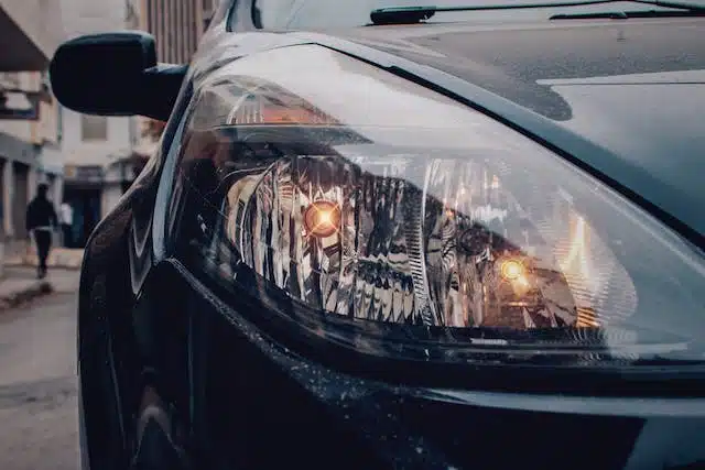 A close up of the headlight of a black car, highlighting its low visibility for road driving.