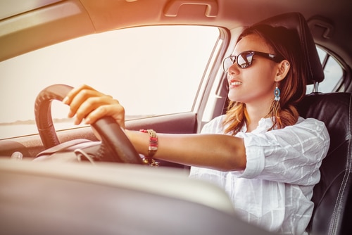 A woman wearing sunglasses driving a car while searching for affordable car insurance options.