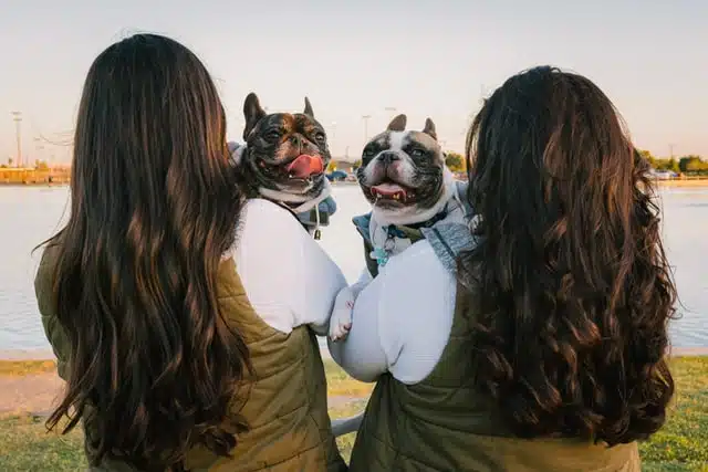 Three women with their dogs enjoying the serene view of a lake.