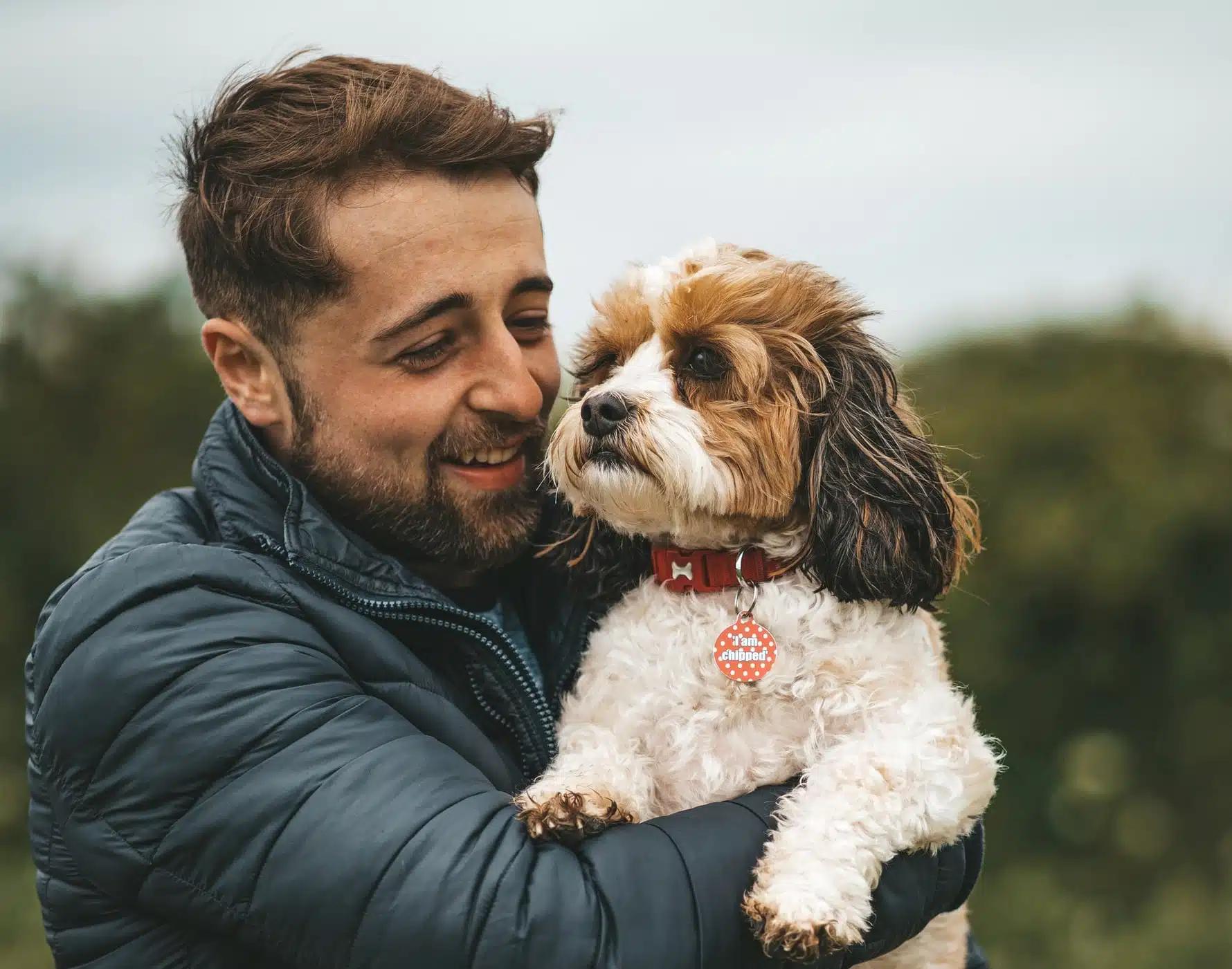 A man holds his fluffy dog affectionately and wonders what pet health conditions he can safeguard it from according to its breed