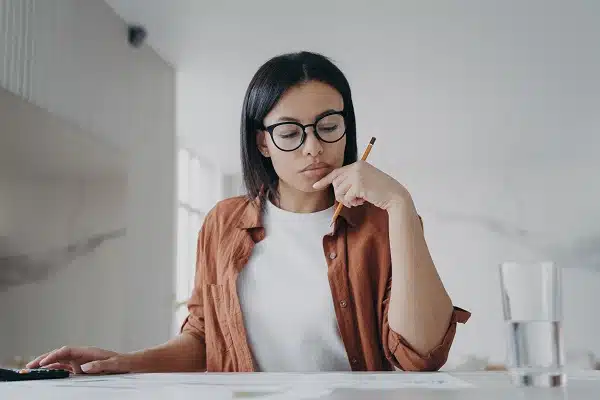A woman sitting at a desk with a calculator and papers, comparing cheap car insurance options.