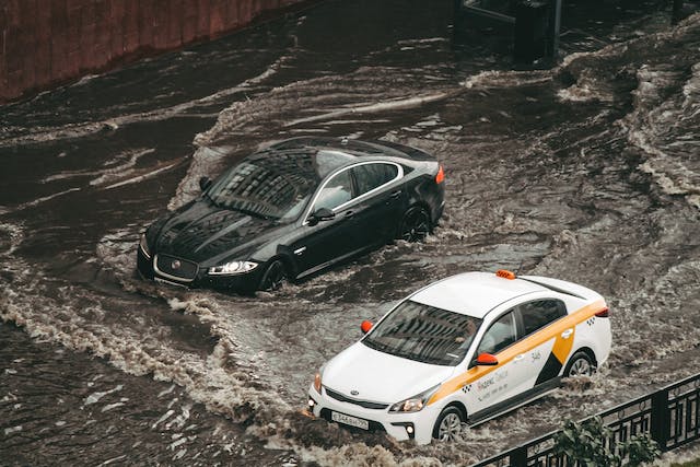 Two cars navigating a flooded street amidst a force majeure event.