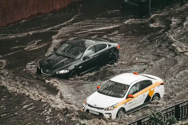 Two cars navigating a flooded street amidst a force majeure event.