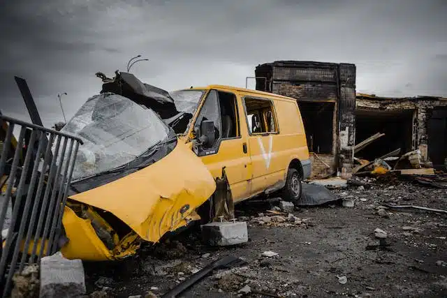 A yellow van sits amidst the ruins of a building, its presence embodying the force majeure of the situation.
