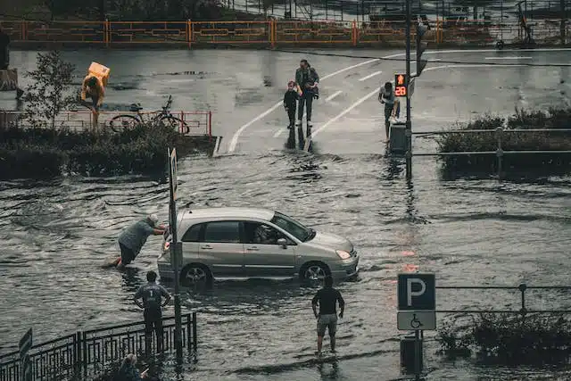 Individuals stranded in a flooded street beside a vehicle.