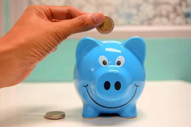 A person saving money by putting a coin into a blue piggy bank.