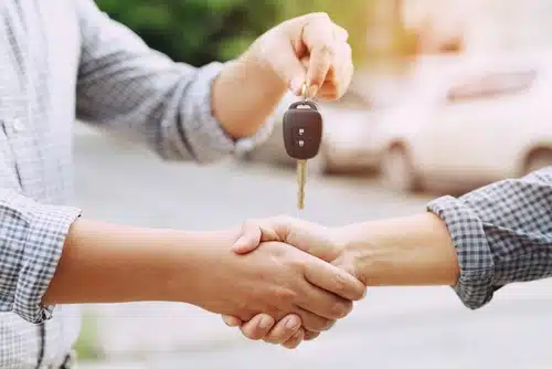 After doing a successful PPSR car history check and making the payment a man shakes hands with a seller and takes the keys to their new car 