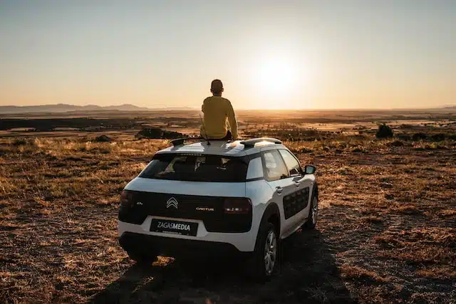 A person enjoying the breathtaking view of a sunset atop a used car, while conducting a car history check for peace of mind with PPSR check.
