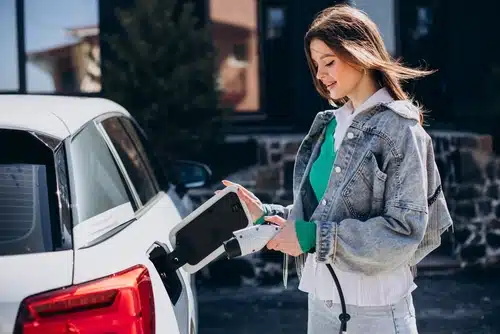 A young woman charges her electric car which she bought with the benefit of an electric car rebate