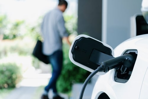 A zero emission vehicle is plugged into a home charging station as the owner walks into his house