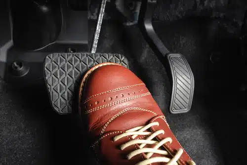 A person in a brown leather shoe is pressing the pedal of a car that won't start and has a stiff brake