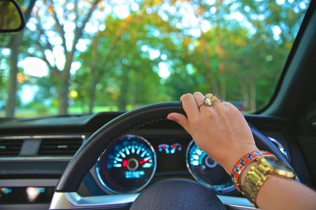 A woman's hand on the steering wheel with the dashboard lights showing everything is working well
