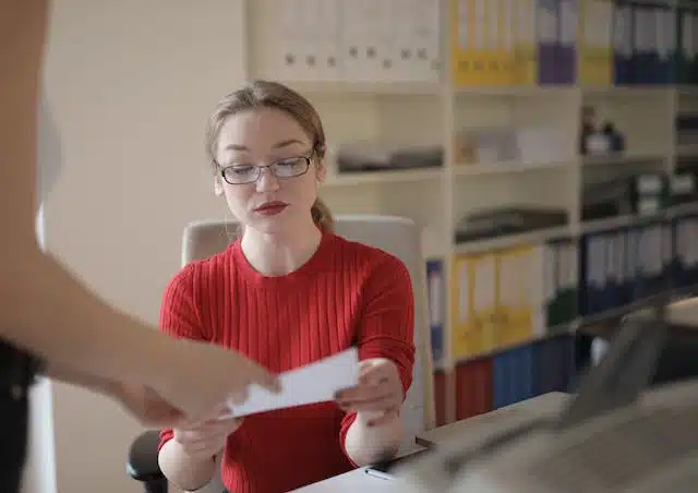 A woman in glasses is handing a letter to another woman in an office, while discussing the Luxury Car Tax threshold in Australia.