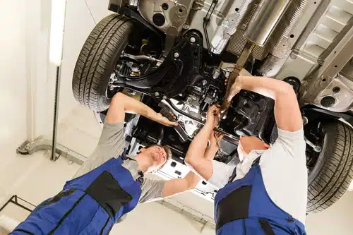 Two mechanics performing a major car service on the underside of a car in Australia.