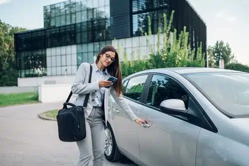 A business woman is standing next to her car, about to drive her car to the mechanic to get a basic car service.