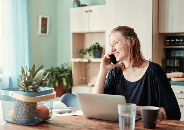 A woman discussing car insurance on the phone while sitting at a kitchen table.
