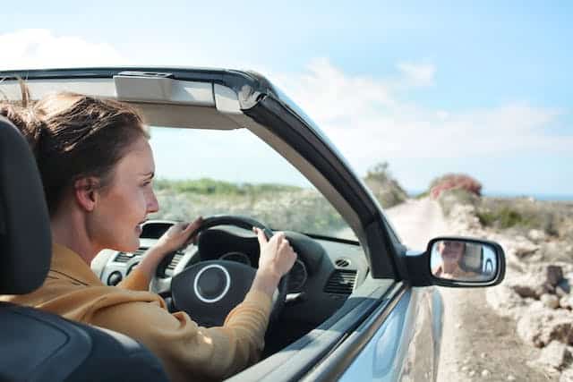A woman driving a convertible car on a holiday road trip, at ease that she's done a full duty of disclosure regarding her car insurance and has the proper protection her plan can provide.