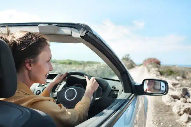 A woman driving a convertible car on a holiday road trip, at ease that she's done a full duty of disclosure regarding her car insurance and has the proper protection her plan can provide.