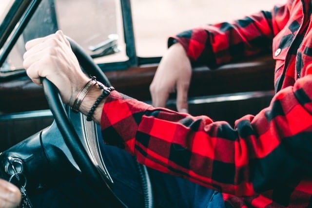 A man driving a car in a plaid shirt feels happy that he's ensured his duty of disclosure for car insurance by letting his provider know about his medical conditions