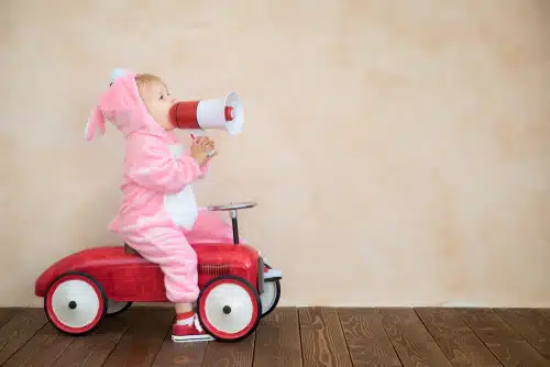 A child in a pink bunny costume promoting Easter road safety while riding a toy car with a megaphone.