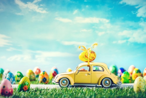 A vibrant yellow car adorned with Easter eggs, driving down the road.