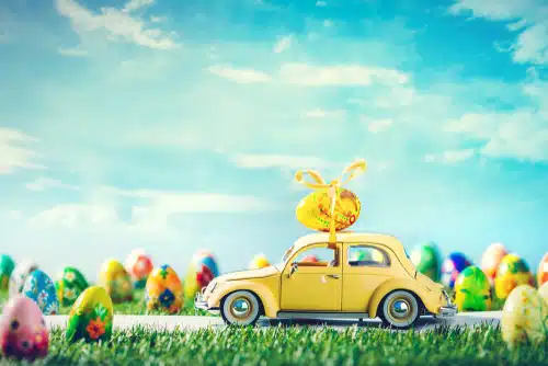 A vibrant yellow car adorned with Easter eggs, driving down the road.